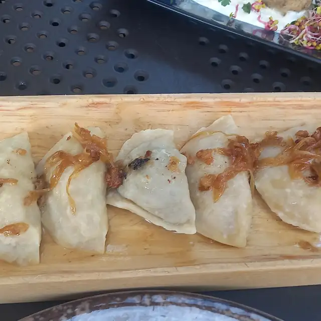 Pierogi ułożone w rzędzie na drewnianej desce, z kiełkami