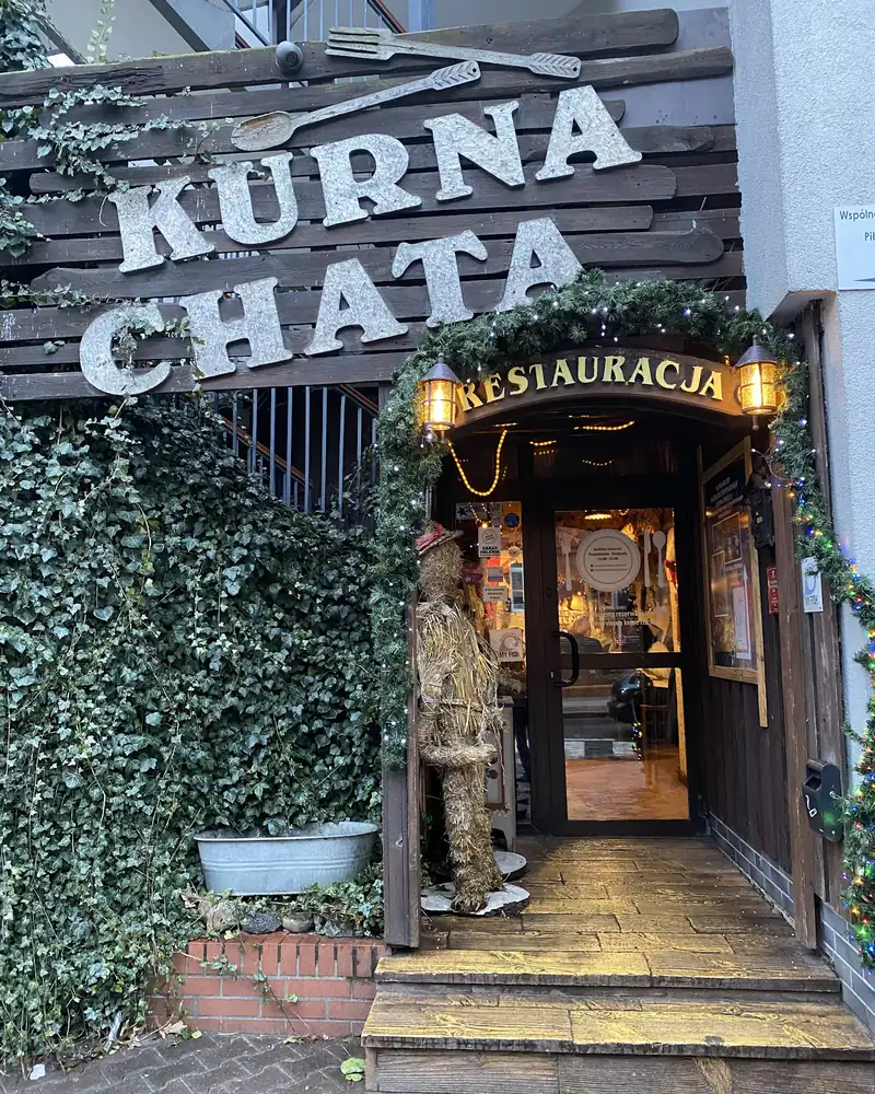 Wejście do restauracji pod drewnianym szyldem KURNA CHATA, obrośnięte bluszczem
